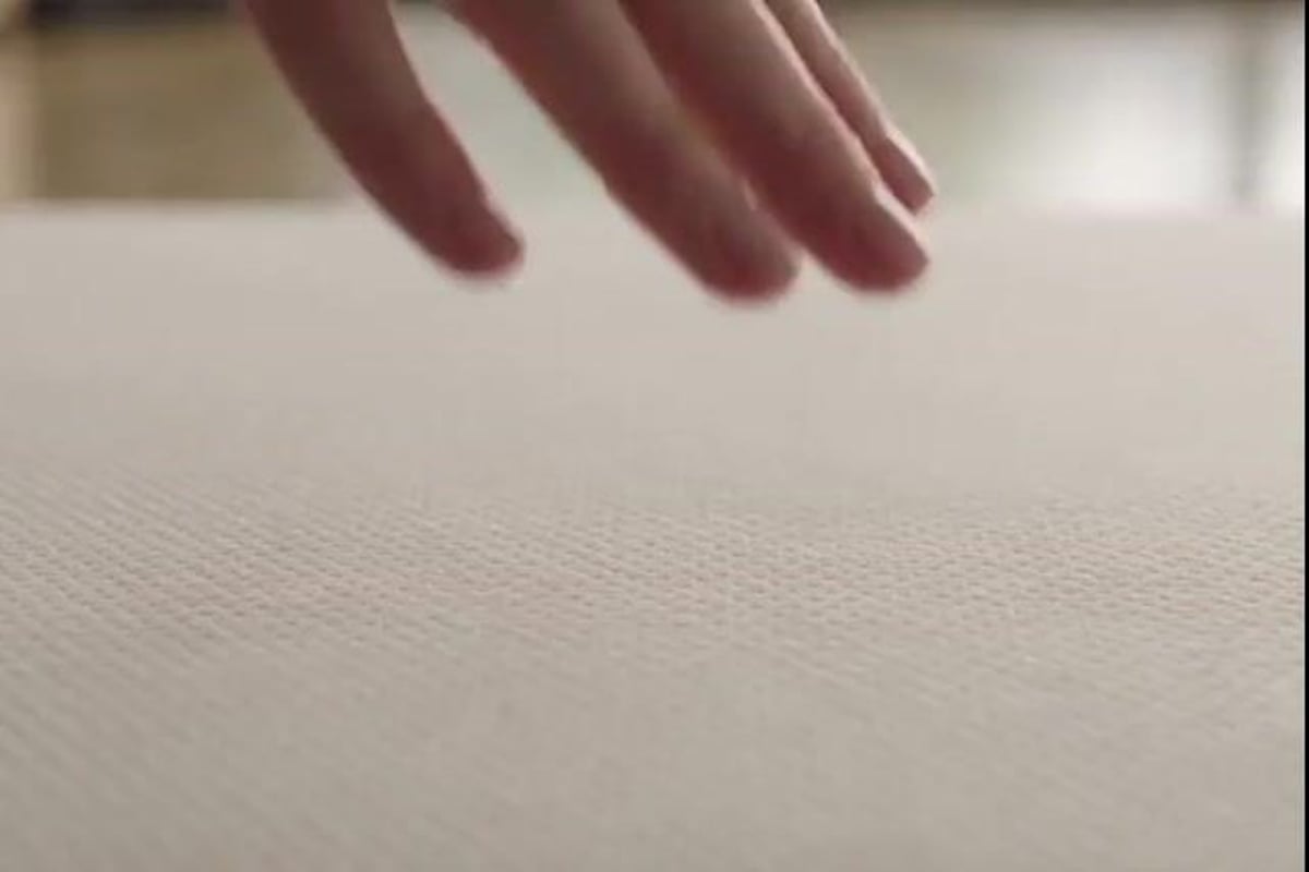 A hand pressing into the top of a white mattress